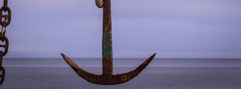 A rusty anchor hanging with the sea in the background.
