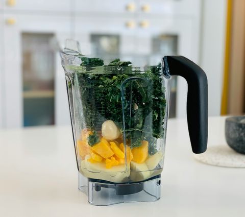 A clear kitchen blender filled with chopped fruit and greens