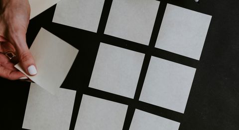 A hand with painted nails placing a white square of paper into a 9 by 9 grid.
